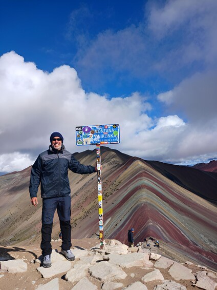 A person standing next to a colorful signpost with a mountain range in the background. 3