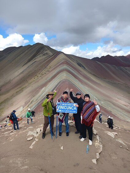 A group of hikers on a mountain trail with a sign indicating Vinicunca. 1
