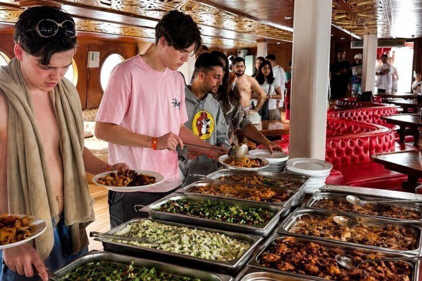 A buffet with various food options, people serving themselves, and a red seating area in the background. 5