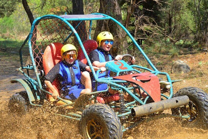 Two people in a blue and red off-road vehicle on a dirt path surrounded by trees. 3
