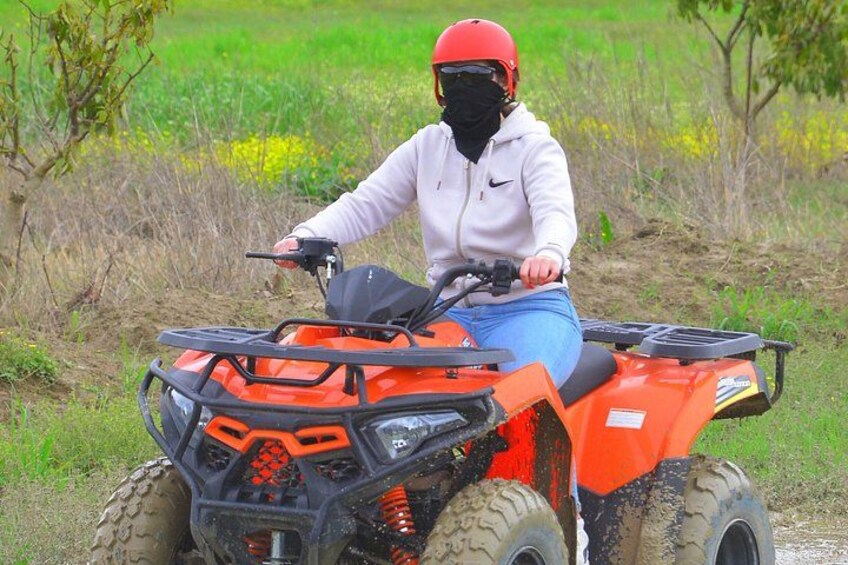 A person riding an orange ATV in a field with green grass and yellow flowers. 3