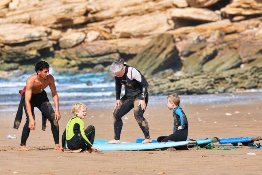 A group of people on a beach with surfboards, rocks, and ocean in the background. 4