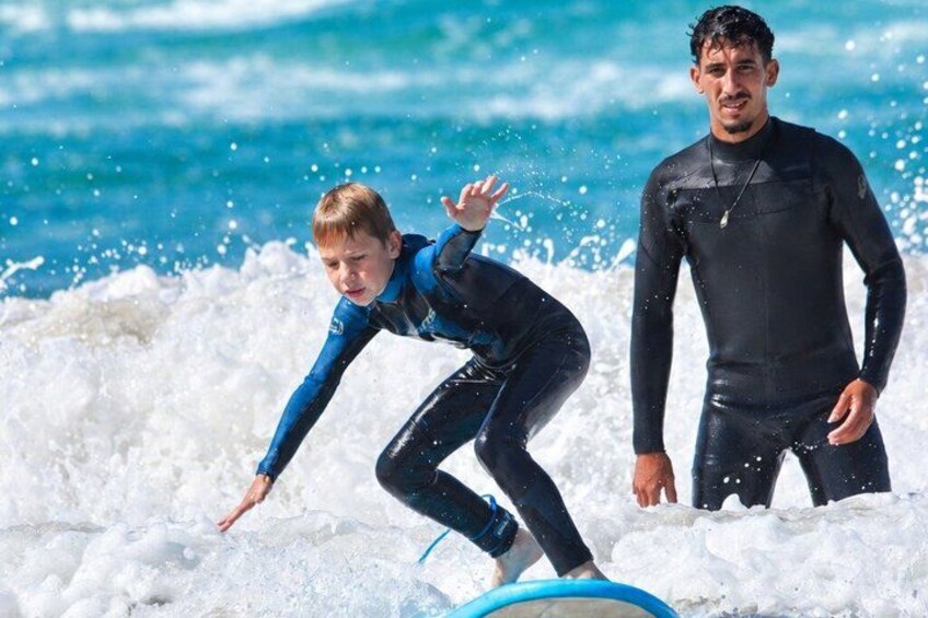 A person surfing on a wave with another person standing nearby. 1