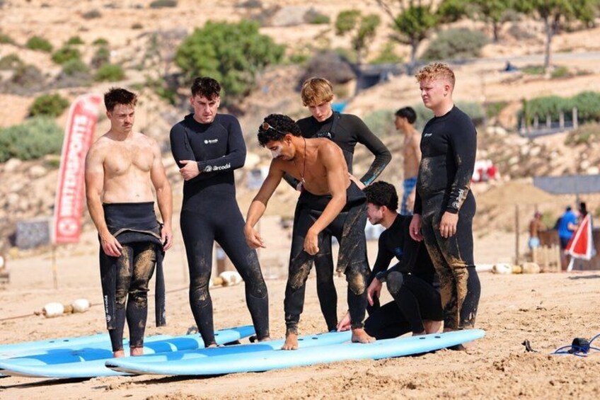 A group of people in wetsuits on a sandy beach with surfboards. 2
