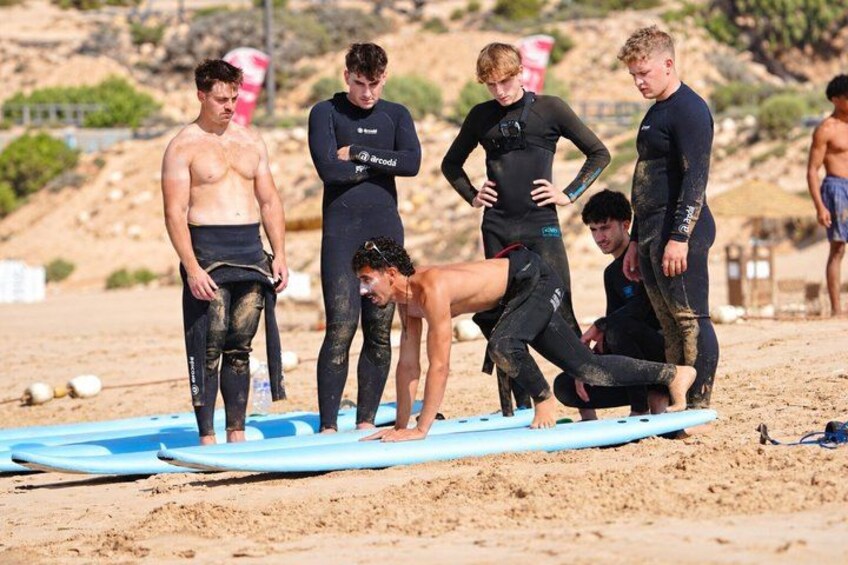 A group of people in wetsuits on a sandy beach with surfboards. 3