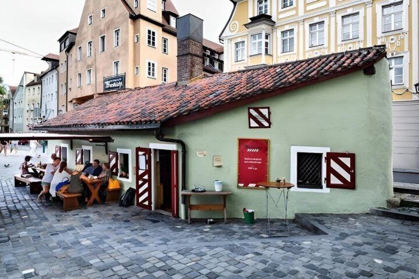 A street with a building that has a red and white striped awning, a sign that says 'Bistro,' and a cobblestone pavement. 4