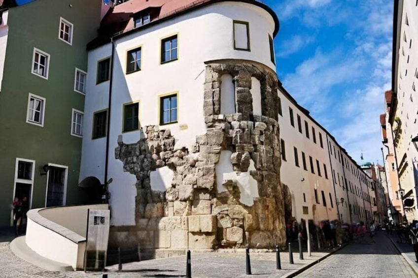 A historic building with a round tower, a cobblestone street, and modern buildings in the background. 3