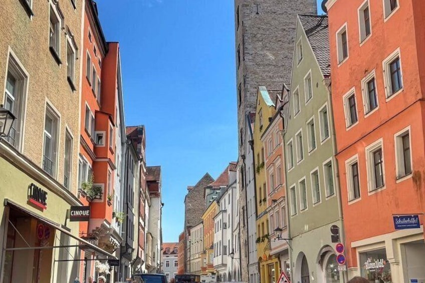 A narrow street lined with colorful buildings, a clear blue sky, and a prominent tower. 2