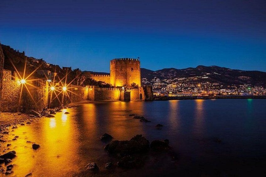 A castle by a calm body of water at night with lights reflecting on the surface. 3