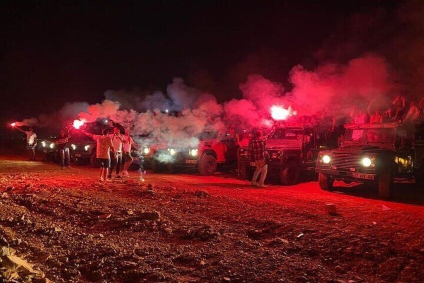 A nighttime outdoor event with people and vehicles, including a truck with a mounted light. 1