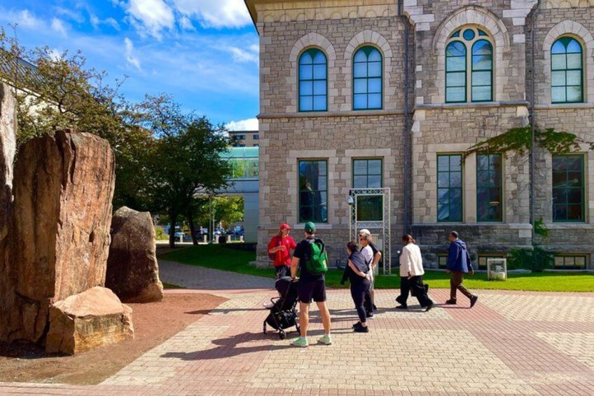 A stone building with arched windows, a paved walkway, and a large rock. 1