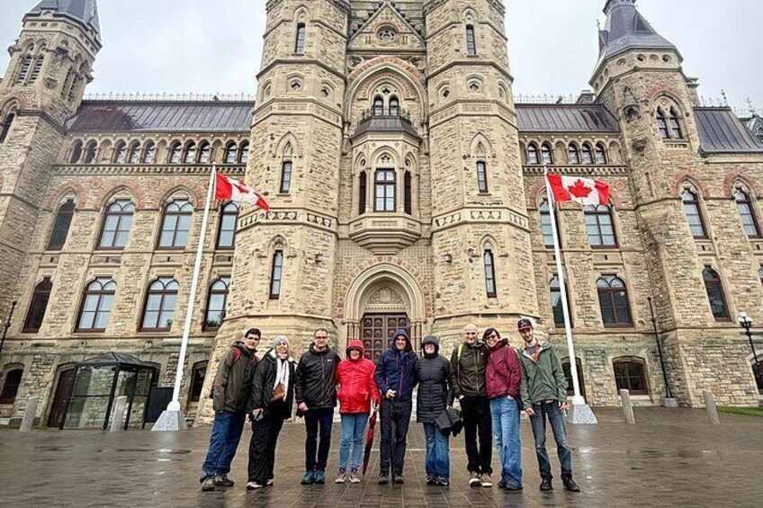 A group of people standing in front of a historic stone building with two Canadian flags. 4