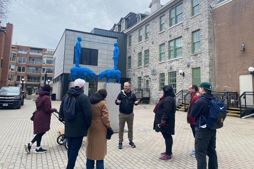 A group of people standing outdoors near a modern building with a sculpture of blue figures. 3