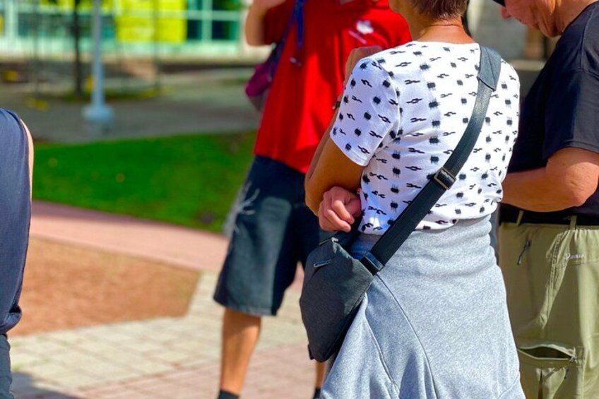 A person wearing a white shirt with black patterns and a grey skirt, carrying a black shoulder bag. 5