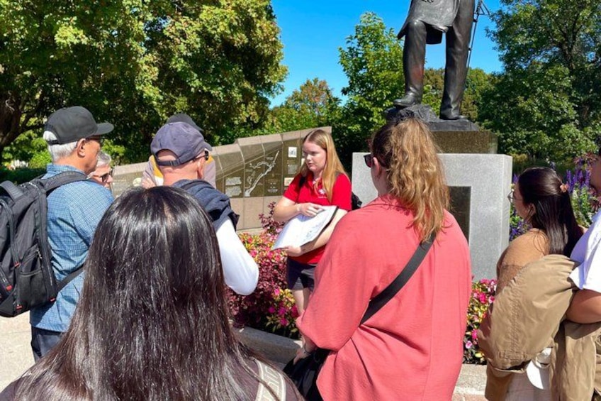 A group of people gathered around a statue in a park with trees and flowers in the background. 1