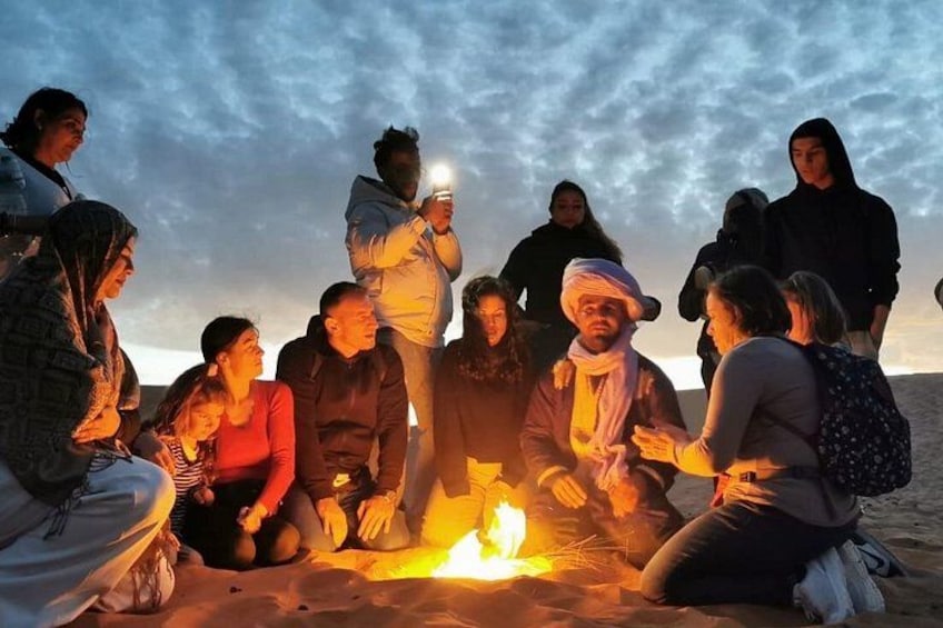 Un grupo de personas reunido alrededor de una fogata en la playa al atardecer. 4