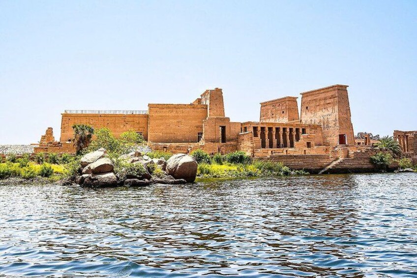 Ancient ruins by a river with large rocks and palm trees. 1