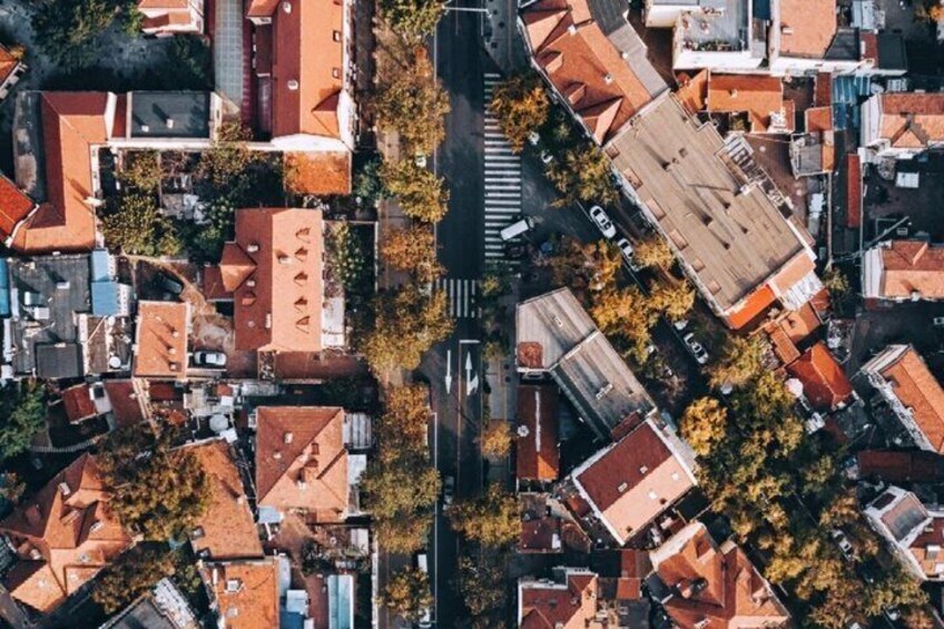 An aerial view of a densely packed residential area with red-roofed houses, a central road, and surrounding greenery. 2