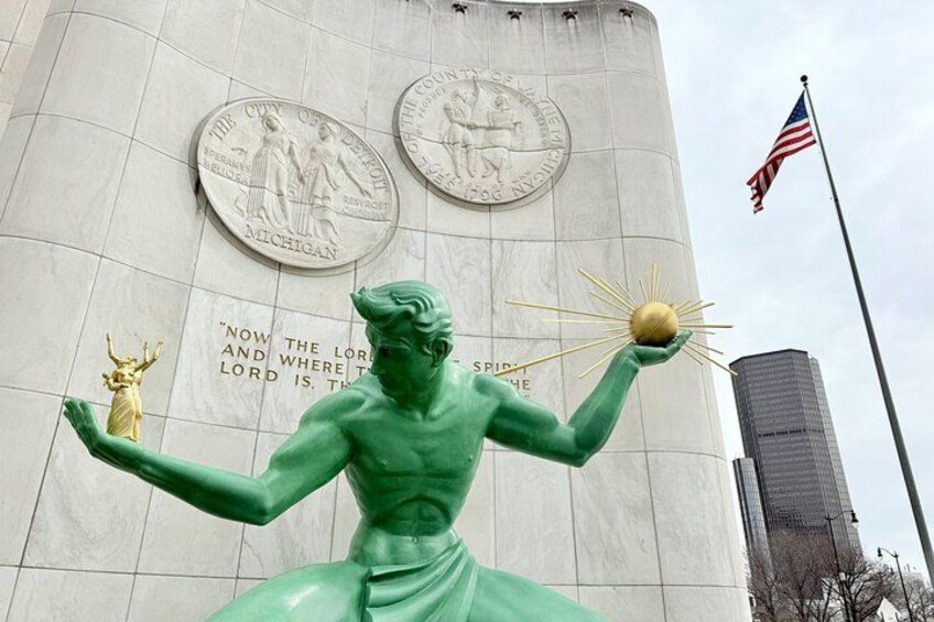 A green statue of a figure holding a sun, in front of a building with plaques and an American flag. 2