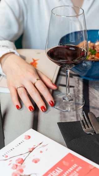 A person with red nail polish resting their hand on a table with a wine glass, a fork, and a menu. 3