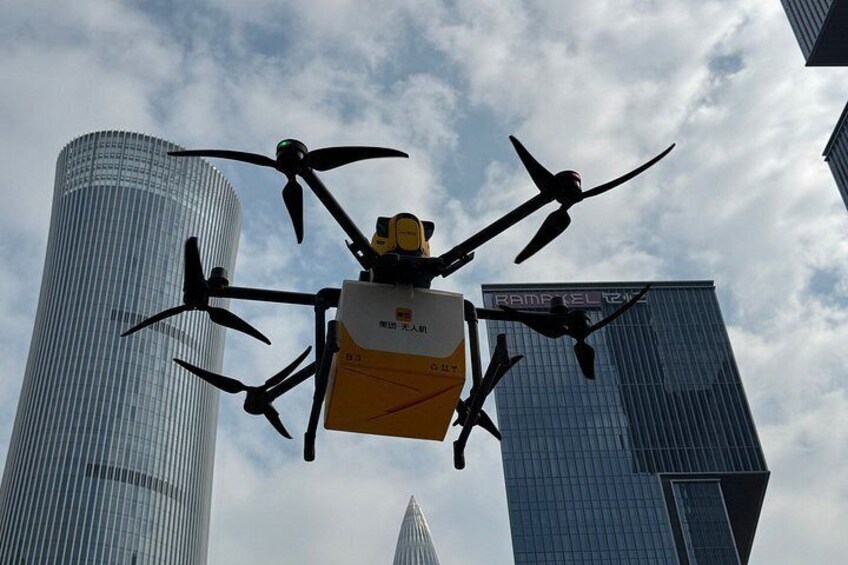 A drone with four rotors flying in front of tall buildings. 1