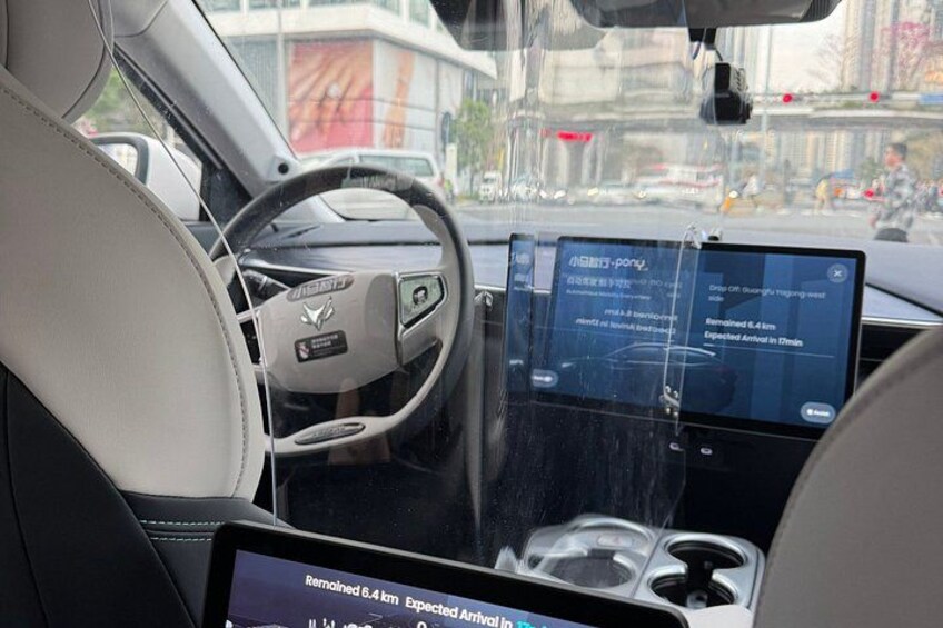 A car interior with a steering wheel, a digital display, and a cup holder. 2