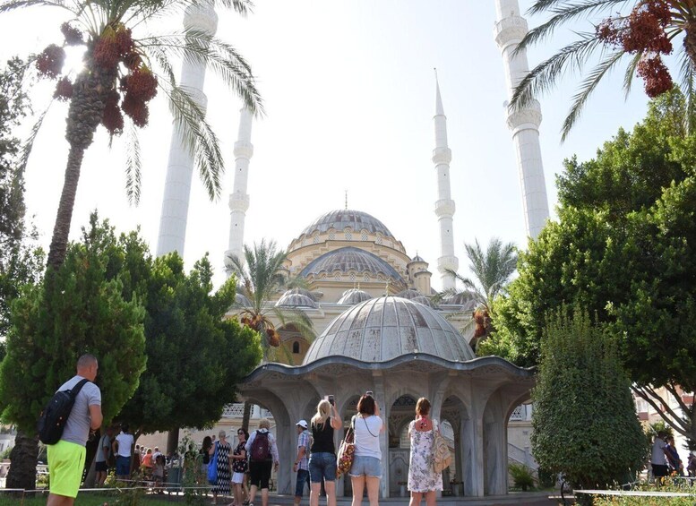 A mosque with a large dome and four minarets, surrounded by palm trees and tourists. 4