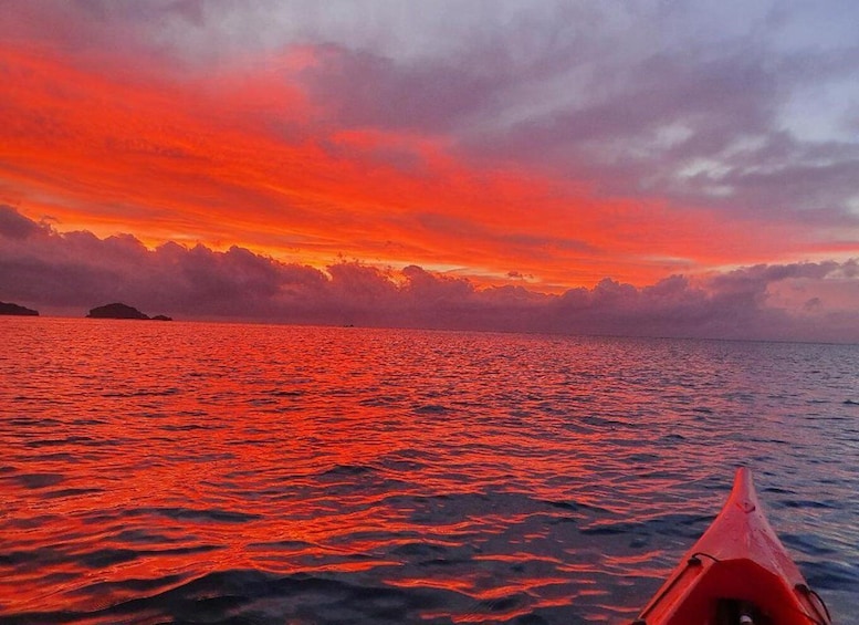 A red kayak on calm ocean waters at sunset with a vibrant sky. 1