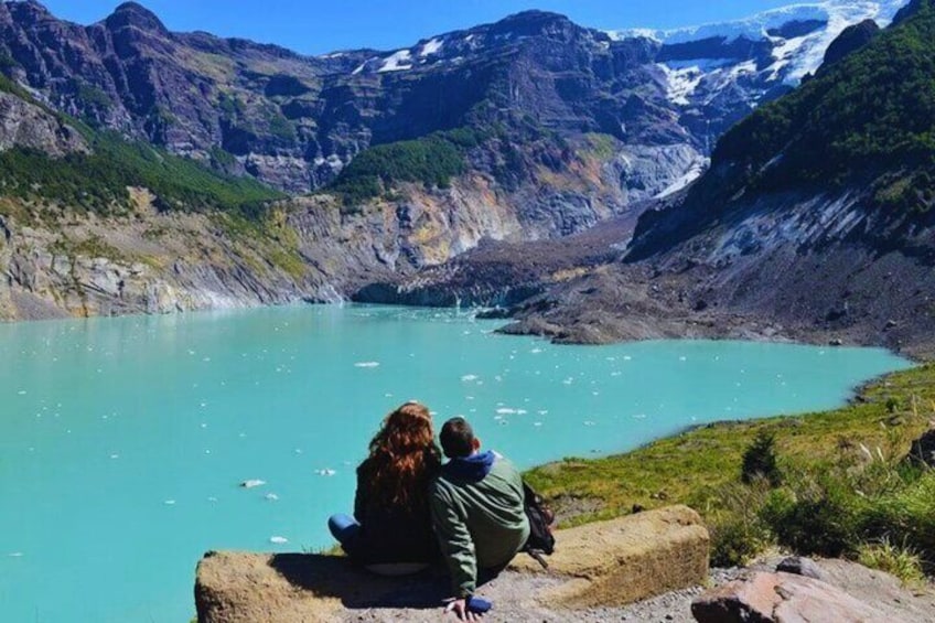 A couple sitting by a turquoise lake with mountains in the background. 1