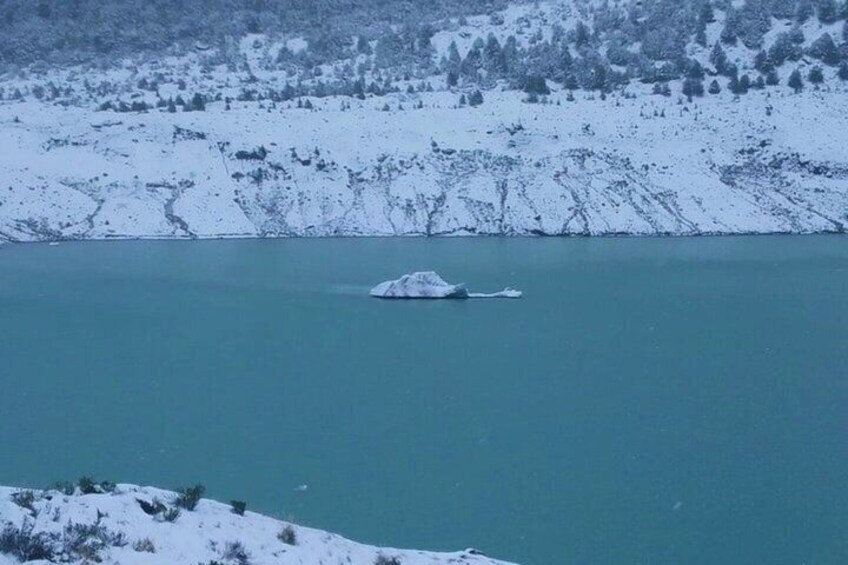 A snow-covered landscape with a body of water and a small ice formation. 4