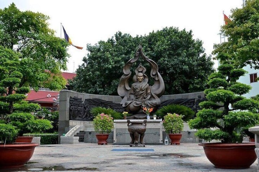 A statue of a deity with multiple arms, surrounded by potted plants and a stone wall. 1