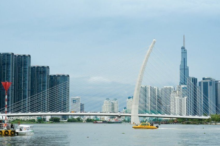 A city skyline with modern skyscrapers, a prominent white cable-stayed bridge, and a yellow boat on the water. 1