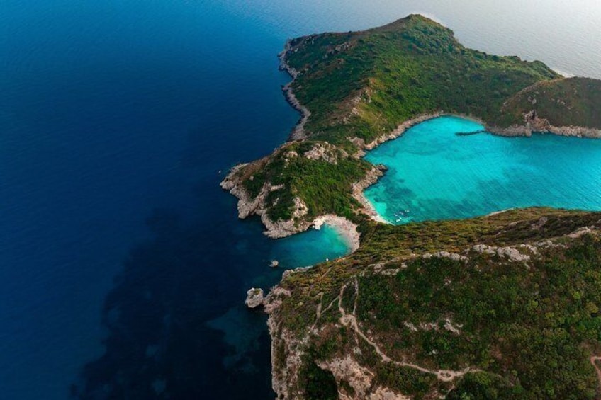 An aerial view of a coastal landscape with a turquoise bay surrounded by green hills. 3