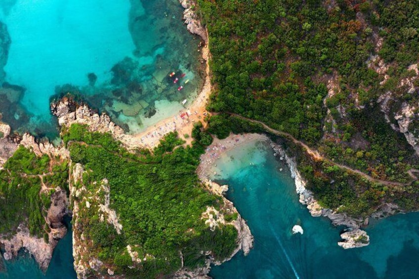 A coastal landscape with clear turquoise waters, a sandy beach, and lush green vegetation. 1