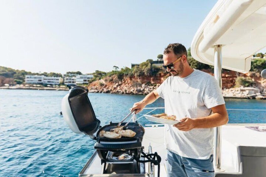 A person grilling on a boat with a coastal landscape in the background. 2