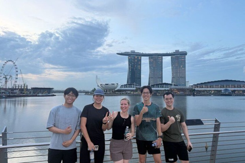 A group of people standing on a waterfront with a Ferris wheel and modern buildings in the background. 2