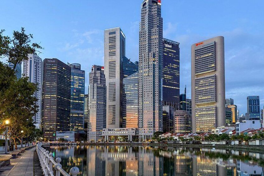 A city skyline with tall buildings, a body of water reflecting the structures, and a pedestrian walkway with a railing. 2