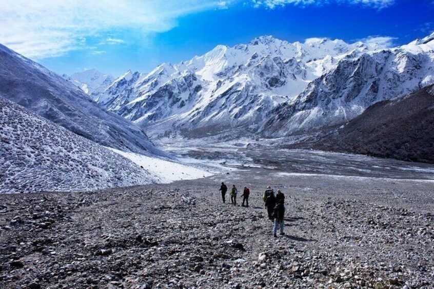 A group of hikers on a rocky mountain path with snow-capped peaks in the background. 2