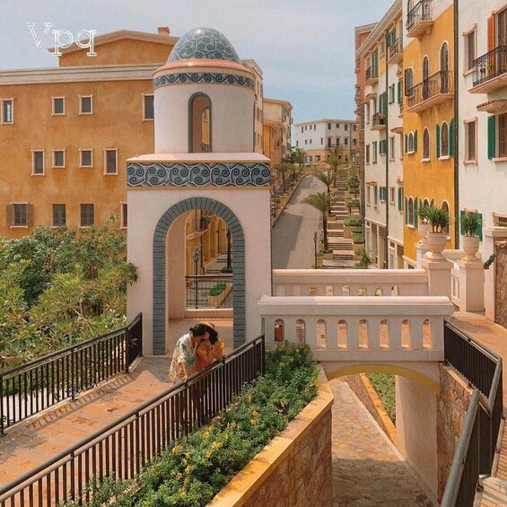 A Mediterranean-style bridge with arches, a domed tower, and terracotta buildings with green shutters. 3
