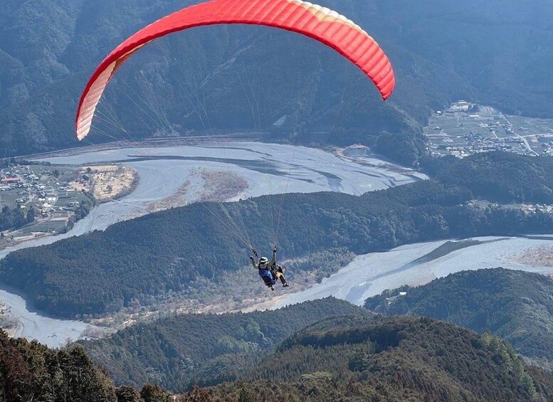 A paraglider over a mountainous landscape with a river and a town below. 5