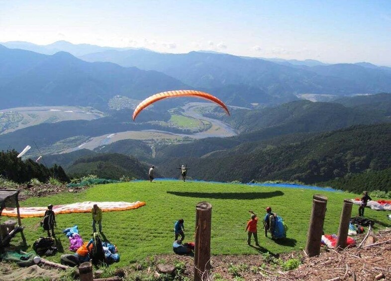 A person paragliding over a green field with mountains in the background. 3