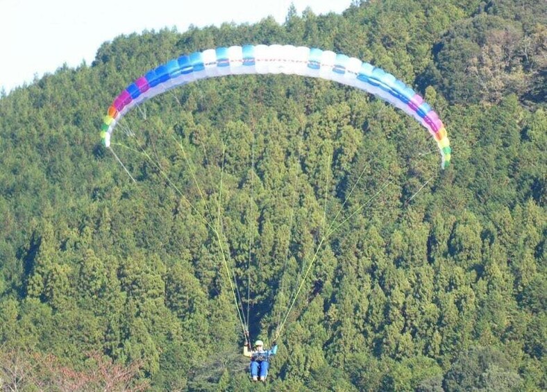 A person paragliding over a forested hill. 2