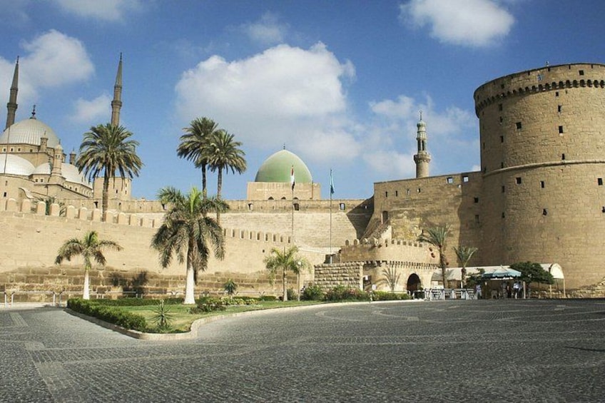A historic building with domes and minarets, palm trees, and a paved courtyard. 5