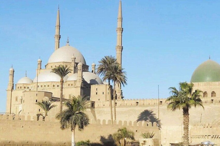 A large mosque with multiple domes and minarets, palm trees in the foreground, and a clear sky. 1