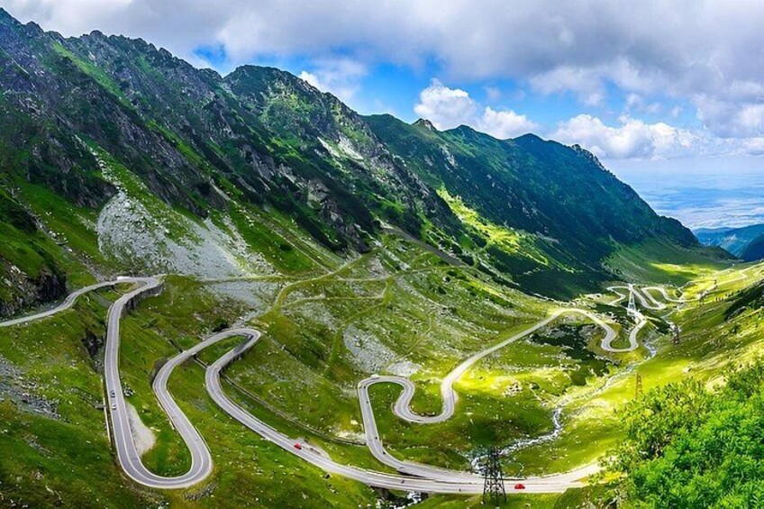 A winding mountain road with green valleys and rocky mountains. 1