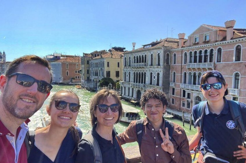 A group of people posing in front of historic buildings with a canal in the background. 1