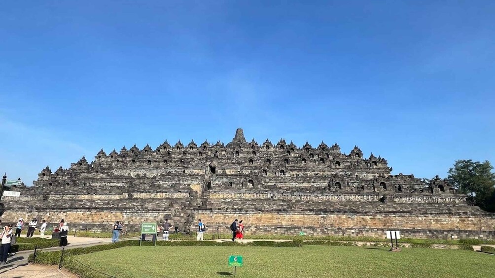 A large, tiered temple with multiple levels and intricate carvings, surrounded by a grassy area with visitors. 4