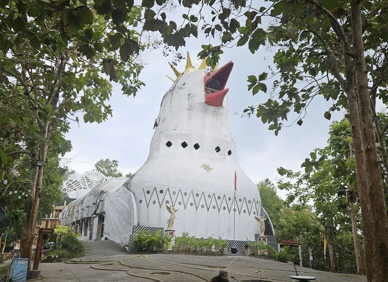 A large white structure resembling a mythical creature with a red interior, surrounded by trees and a covered building. 3