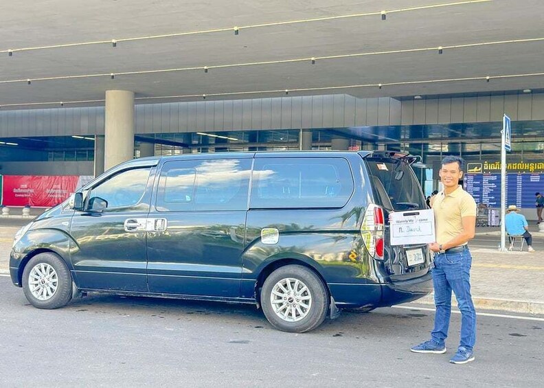 A man standing next to a dark green van with a sign on the back. 4