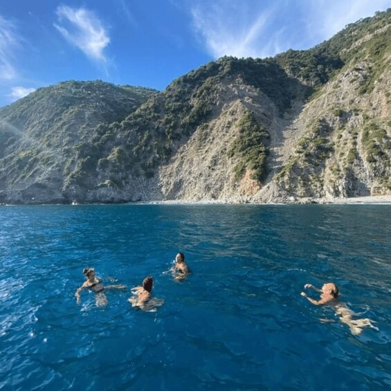 Four people swimming in a clear blue sea with rocky hills in the background. 2